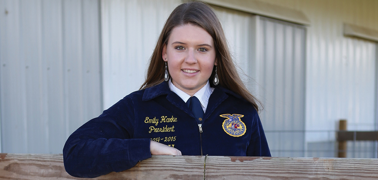 Emily Harke stands at a fence wearing official dress FFA attire. 