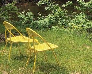Yellow metal chairs sitting on bank of river in the upper peninsula in summer.