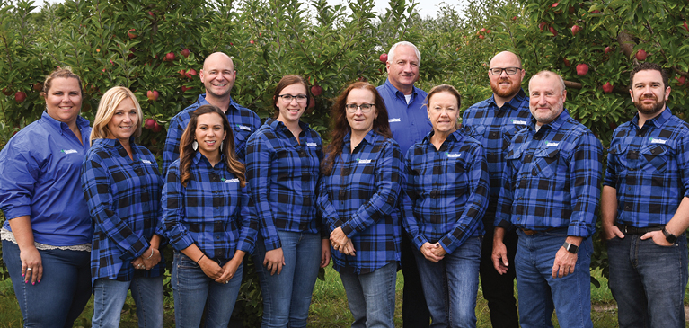 GreenStone Farm Credit Services fruit crop team standing in blue and black flannels in front of apples trees at a customer farm.