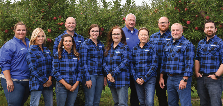 GreenStone Farm Credit Services fruit crop team standing in blue and black flannels in front of apples trees at a customer farm. 