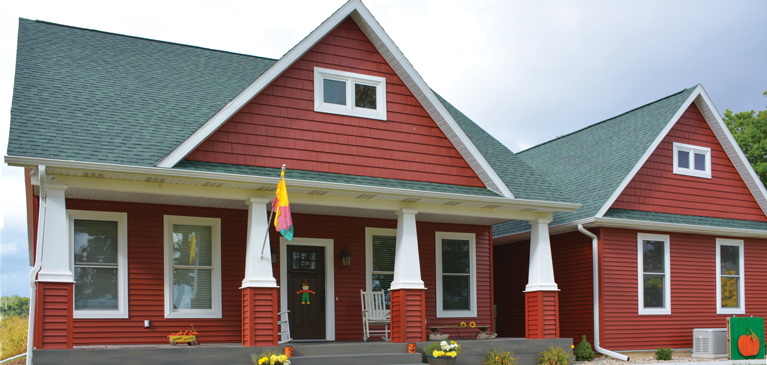 Beautiful, customer-built, red house with front porch decorated for fall on over 40 acres of land.