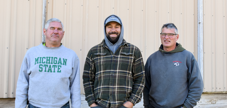 Three men in front of tan barn