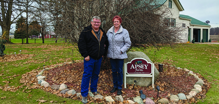 Allen and Kathy Apsey stand in from of farm sign.