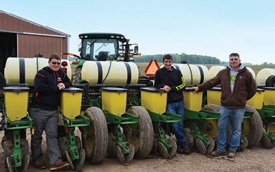 Three farmers standing in between farm equipment