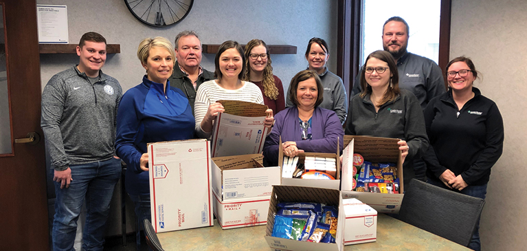 Employees pose with goodies for the troops. Updated.