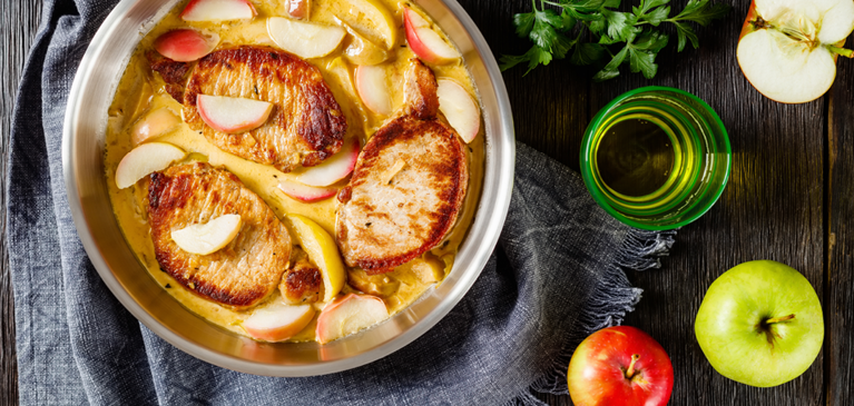 Apple cider braised pork shoulder in bowl with apples on the table