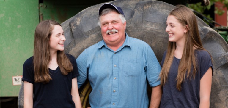 Grandfather standing in front of a tractor tire with two granddaughters