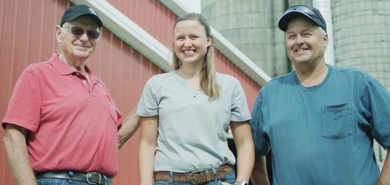 Five generation dairy farmers, grandfather, father, daughter stand outside in front of silos on the farm
