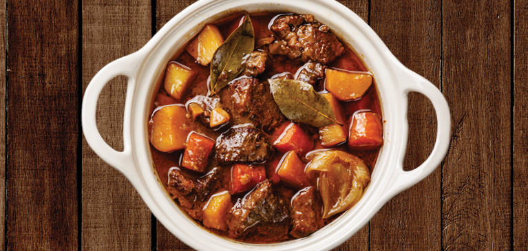 Bowl of beef stew from above with carrots, potatoes, beef and leaves in broth.