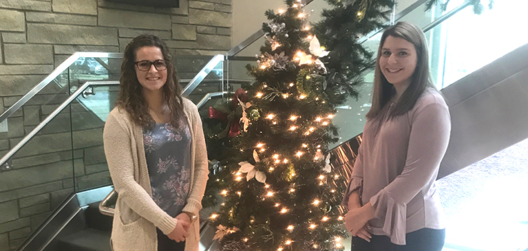 Lauren Voelker and Cameron Cook standing next to a Christmas tree in GreenStone lobby