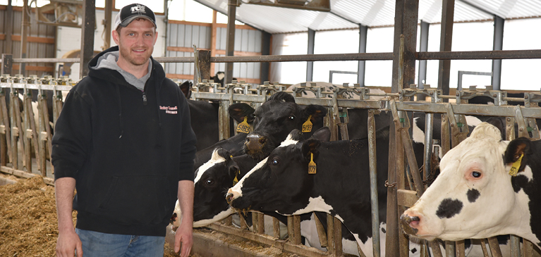Man standing in dariy barn in front of cows smiling 