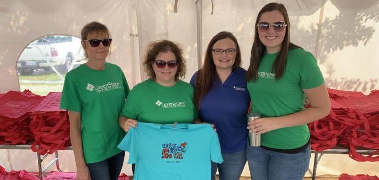 GreenStone employees pose for picture with blue t-shirt while setting up race for 5k run and walk.