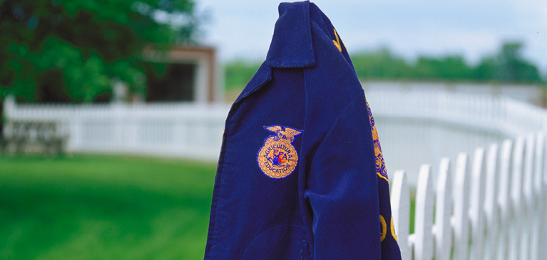 FFA blue jacket hanging on fence post in field