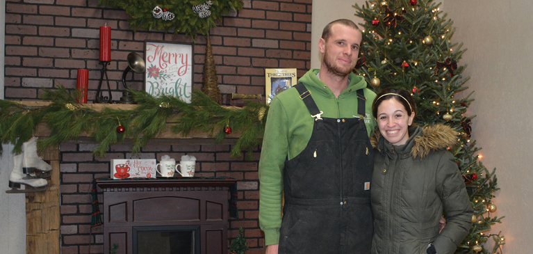 Photo of couple in front of fireplace with Christmas decorations and Christmas tree.