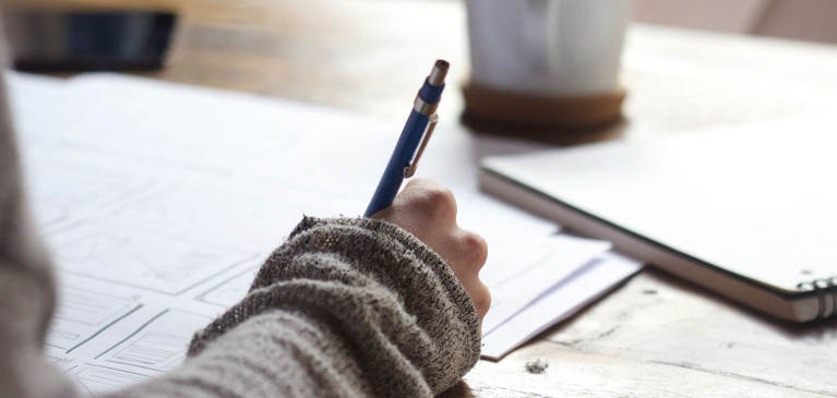 Person taking notes with a coffee cup in the background