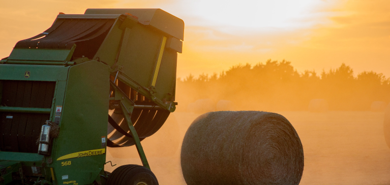 Haybailer in field at sunset