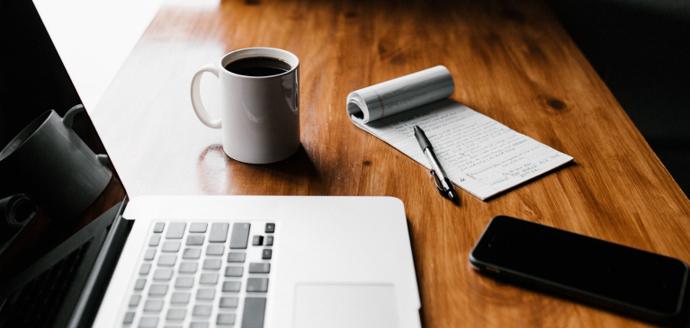 Desk with computer, coffee, and note pad.