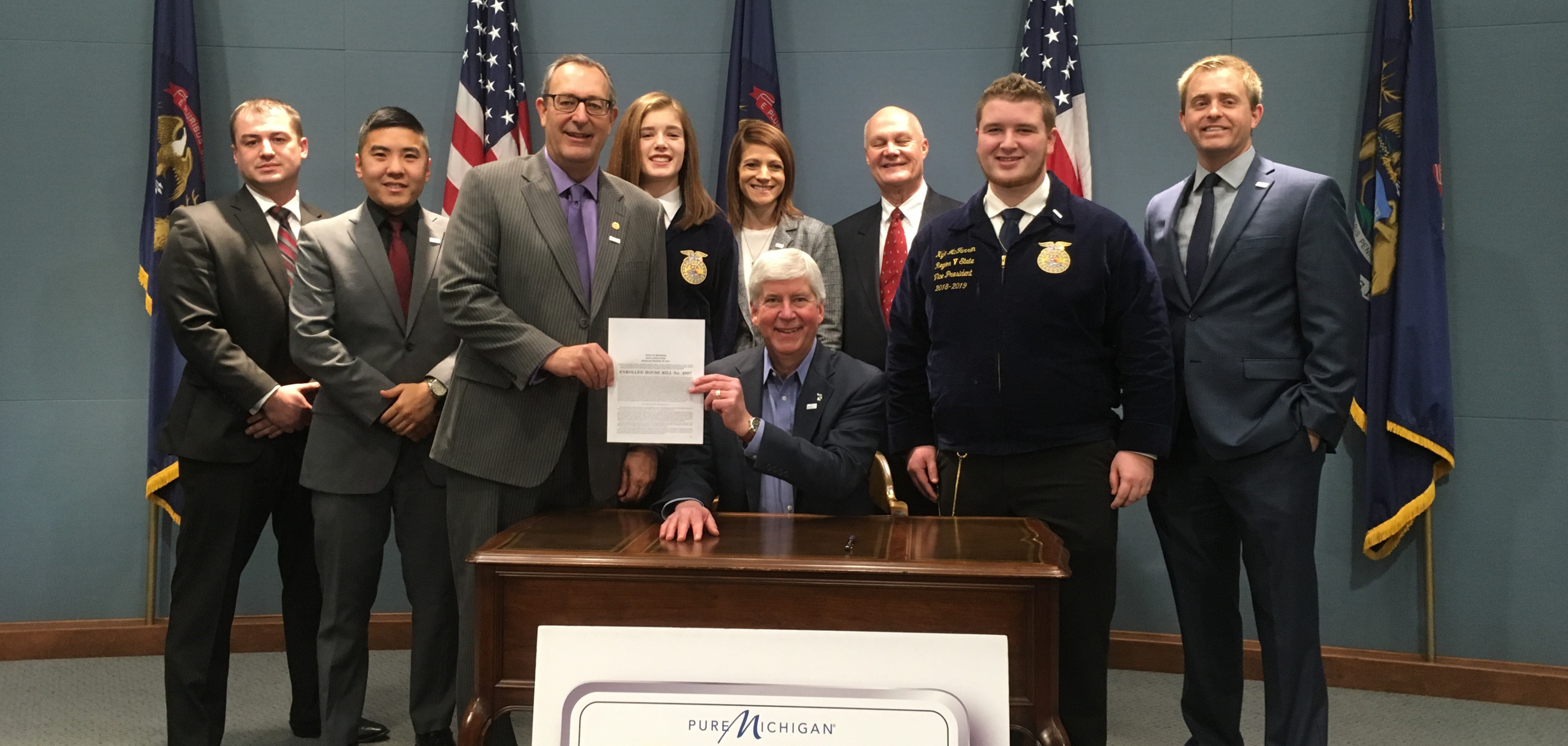 Photo of people standing behind Governor Rick Snyder at ceremonial bill signing.