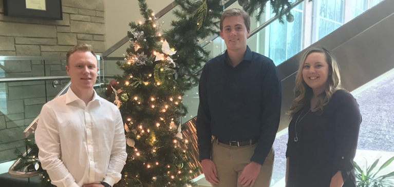 Devon Herzig, Phil Sloss, and Paige Soukup standing by a Christmas tree in the GreenStone East Lansing office lobby