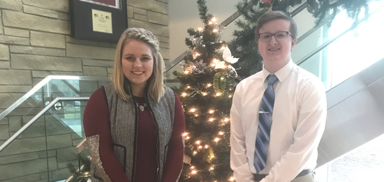 Amber Echlin and Jeffrey MacCowan standing by Christmas tree in GreenStone lobby