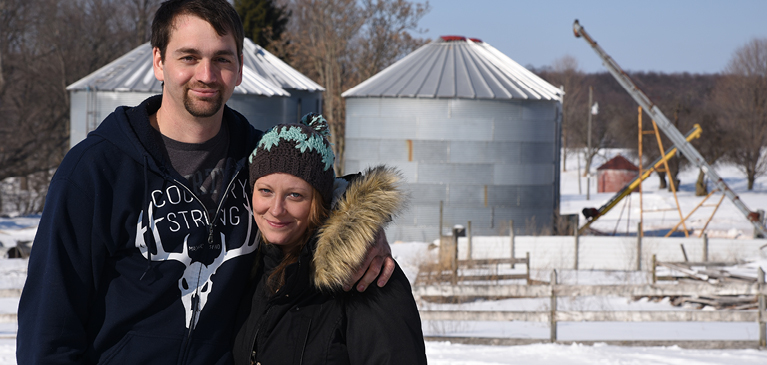 Michigan couple standing in front of oil drilling machines in snowy weather