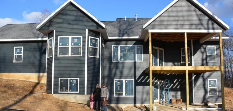 Newly built large two story house with family of four standing in front.