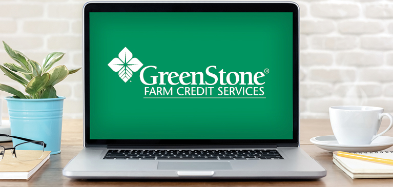 Silver laptop open with screen displaying GreenStone logo on a greenbackground