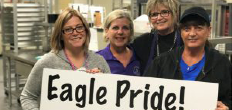 Schoolcraft lunch employees holding sign in cafeteria that says Eagle Pride