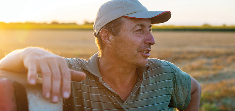 Male farmer leaning on tractor in a field with the sunsetting in the background. 