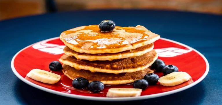Blueberry pancakes stacked on red plate covered with syrup and butter