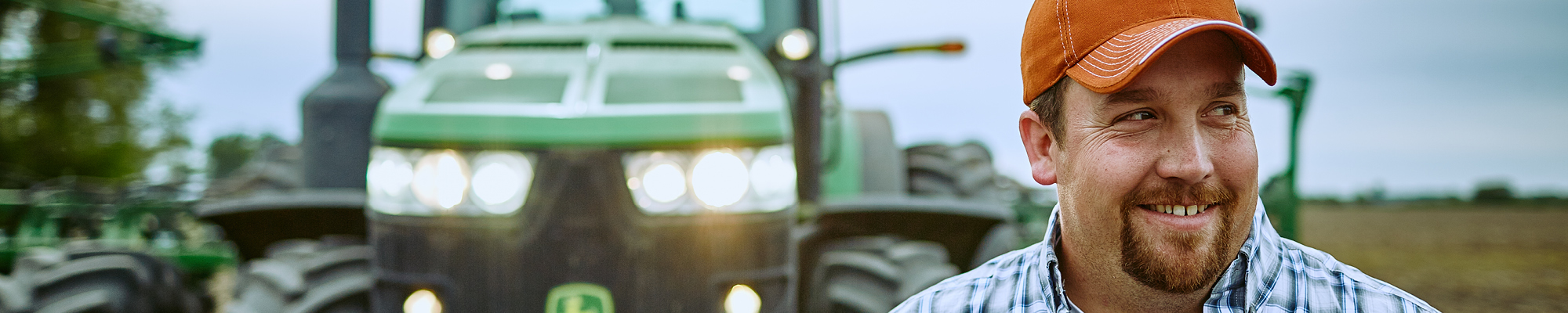 Farmer smiling standing in a field with a tractor