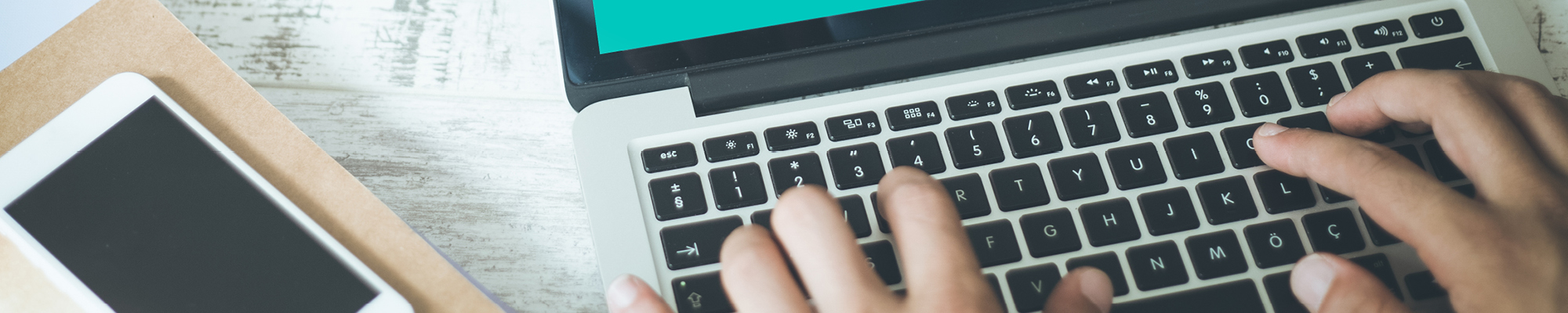 Hands typing on a laptop computer with a smart phone nearby