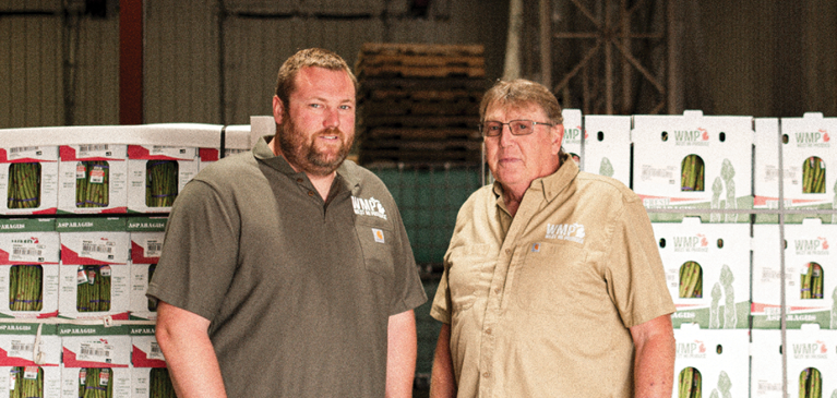 Nick and Ken stand in front of asparagus in their packing facility