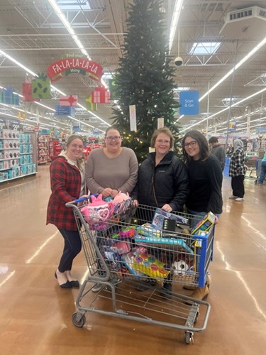 Four women standing behind a shopping cart full of toy donations.