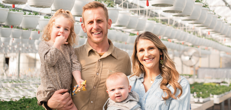 Young family of four stands in a greenhouse