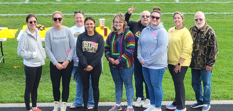 A group of people standing on the track around a football field posing for a picture