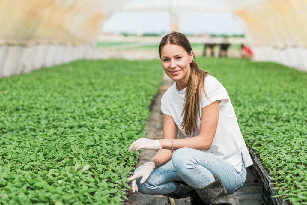 A woman crouching down to tend to small plants in a greenhouse.