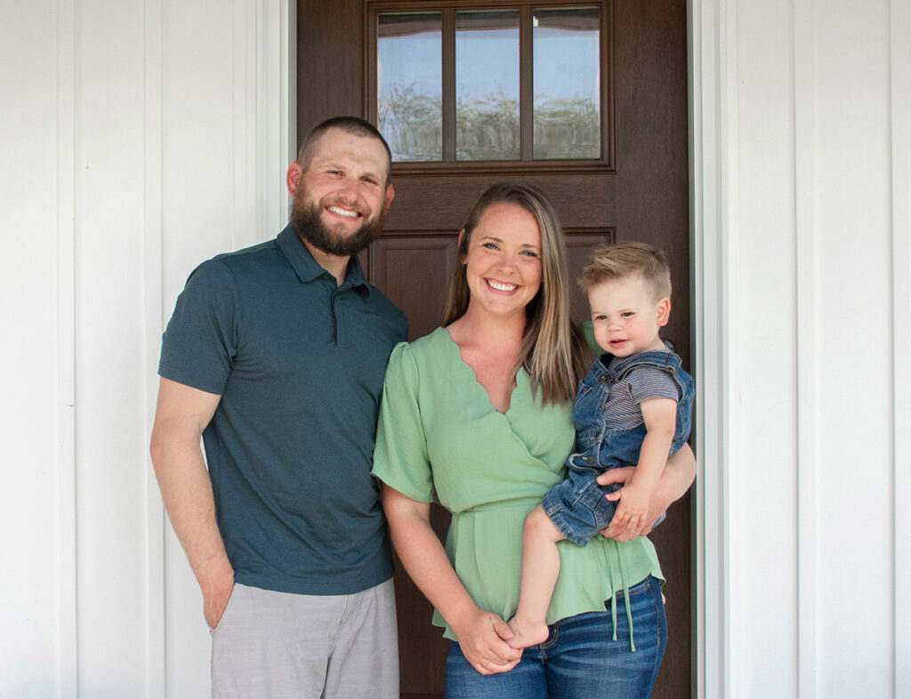 Taylor Schomaker standing in front of a house door with his wife and kid.