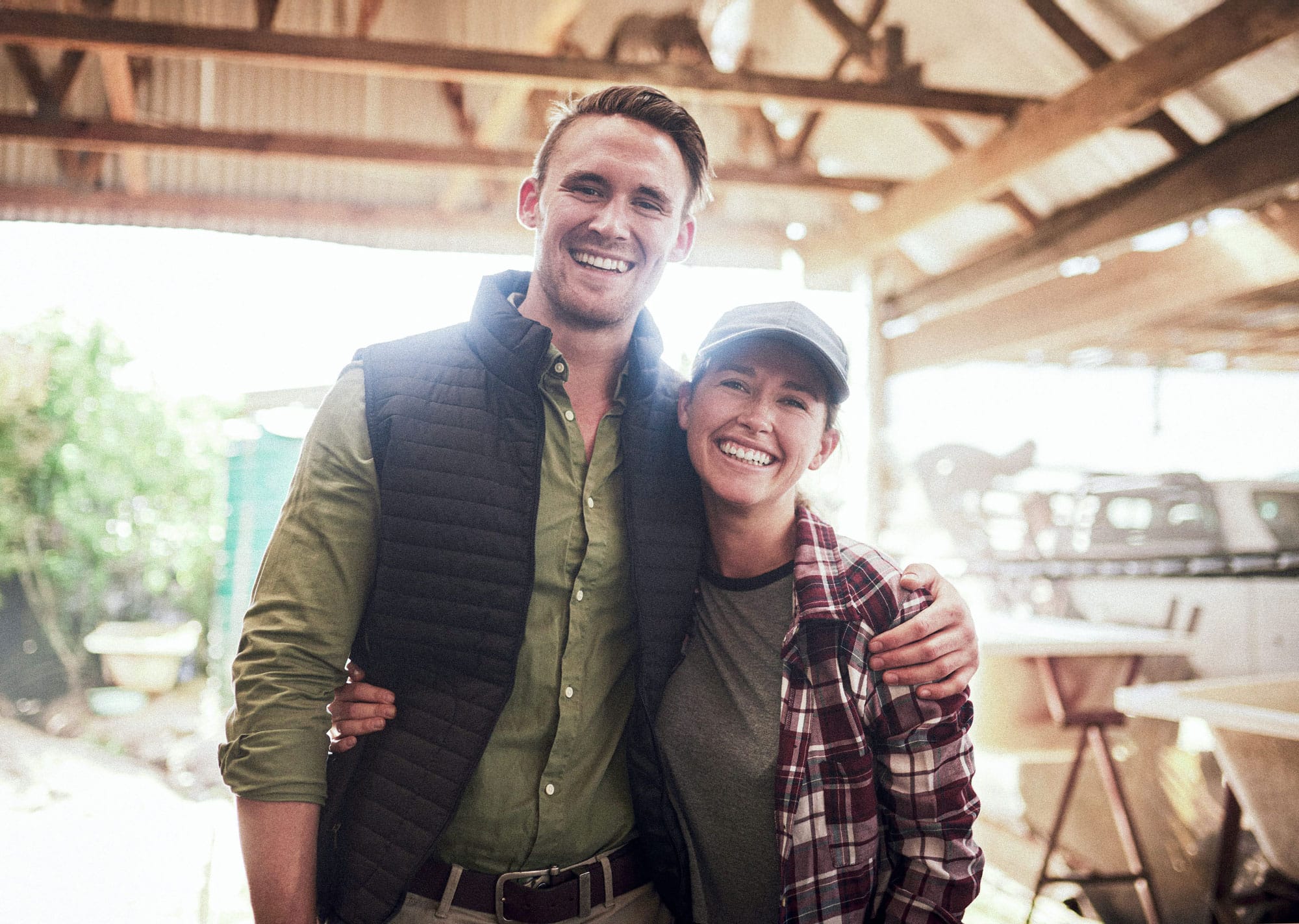 A young couple smiles for the camera from inside a barn.