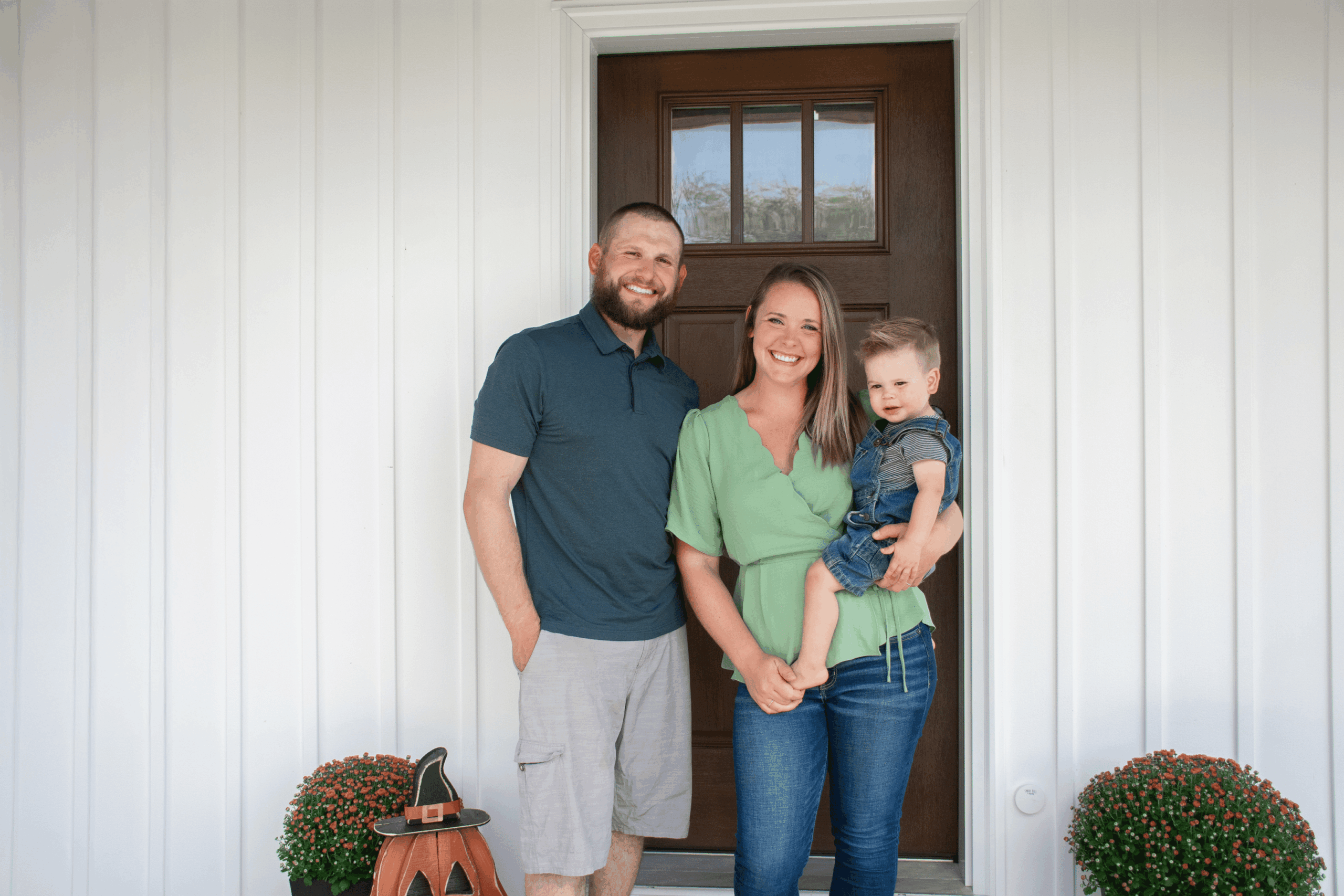 Taylor Schomaker standing in front of a house door with his wife and kid.