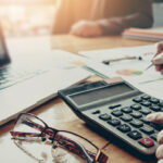 Man using calculator on desk with papers and computer