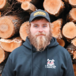 Man in front of stack of logs