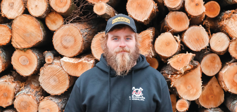 Man in front of stack of logs