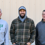 Three men in front of tan barn